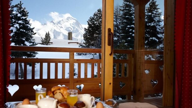 Bandeja de desayuno con huevos, tostadas y jugo en un balcón con vista a una montaña nevada.