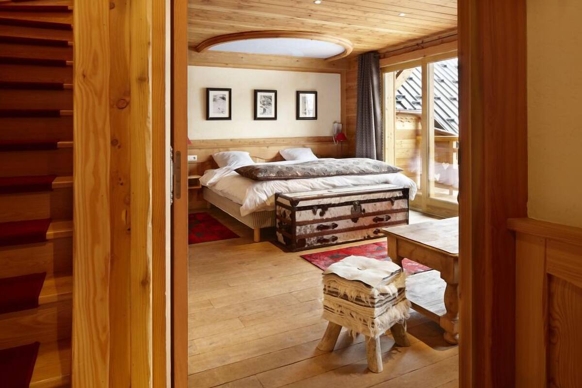 Una habitación de madera con una cama, un taburete pequeño y una mesa. Hay tres cuadros enmarcados en la pared.