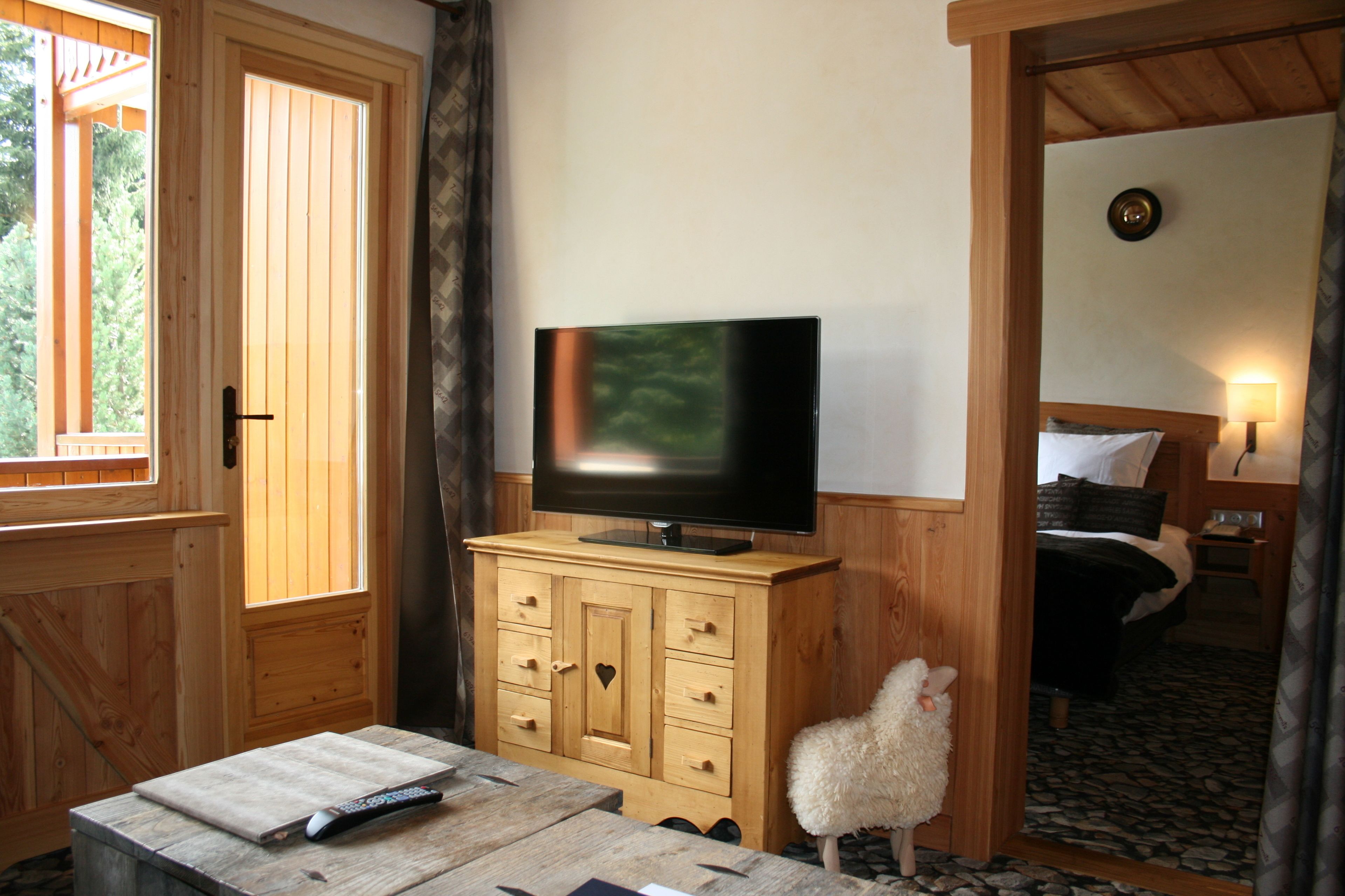 Ein Holzblockhaus-Interieur mit einem Fernseher auf einem Schrank, einer Fernbedienung auf einem Tisch und einem flauschigen weißen Schaf im Durchgang.