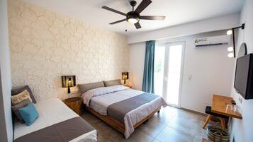 A bedroom with two beds, a ceiling fan, a desk, a TV, and a window with curtains.