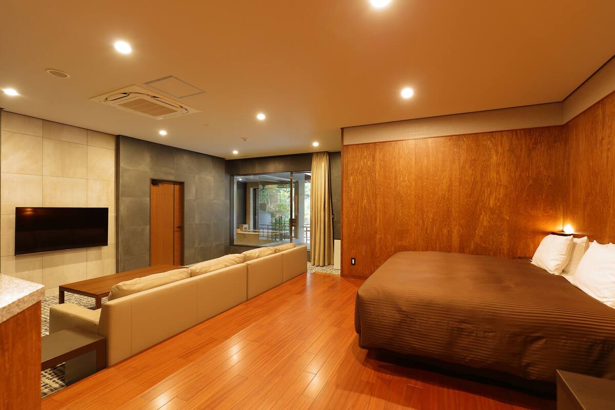 Una habitación de hotel moderna con una cama grande, un televisor de pantalla plana en la pared, un sofá y piso de madera.
