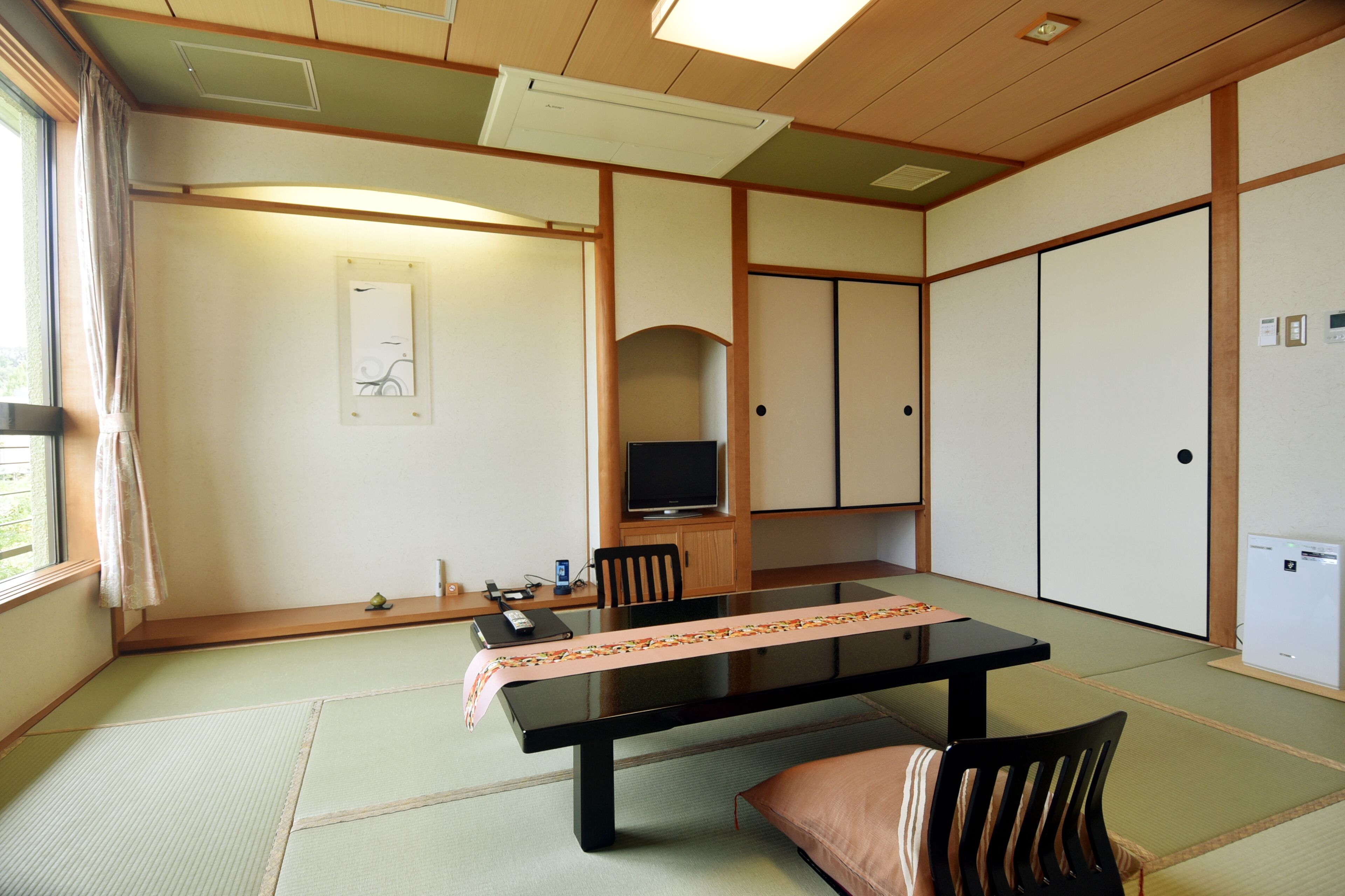 A traditional Japanese-style room with tatami flooring, a low table with a table runner, a television, and sliding doors.