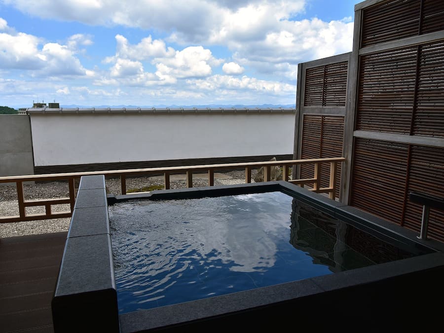 A rooftop pool with a view of the city skyline, surrounded by a wooden fence and a stone wall.