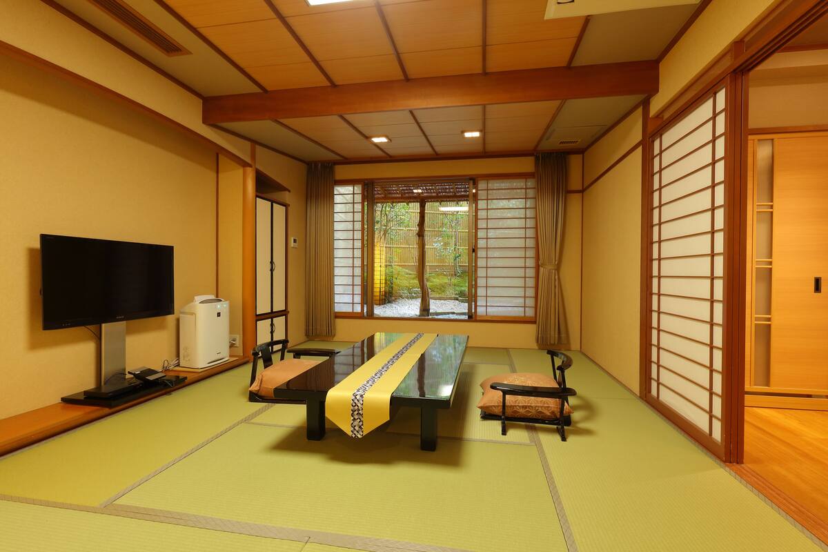 Una habitación tradicional japonesa con suelo de tatami, una mesa baja de tatami, un televisor y una puerta corrediza con paneles shoji.