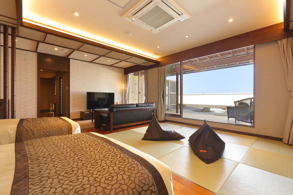 Habitación de hotel con dos camas, un televisor y un amplio ventanal con vista a la playa.