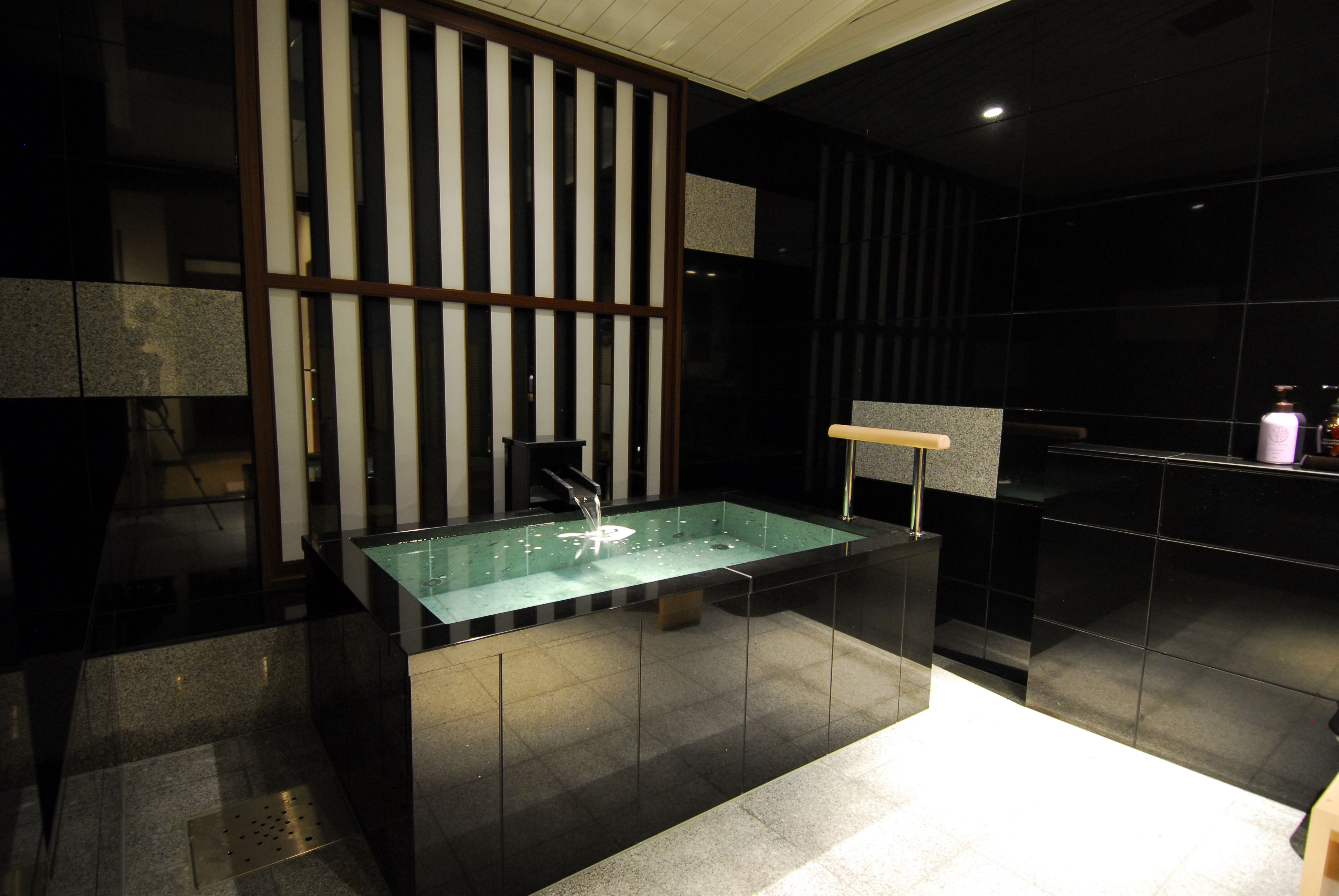 A modern bathroom with a rectangular glass sink, black tiled walls, and a wooden partition.
