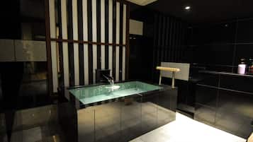 A modern bathroom with a rectangular glass sink, black tiled walls, and a wooden partition.