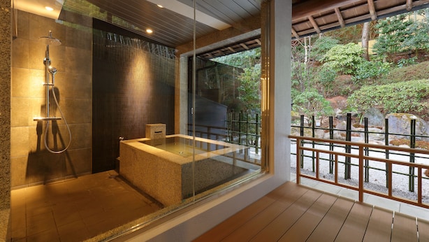 Un baño moderno con ducha acristalada, una bañera independiente y vistas a un jardín ajardinado.
