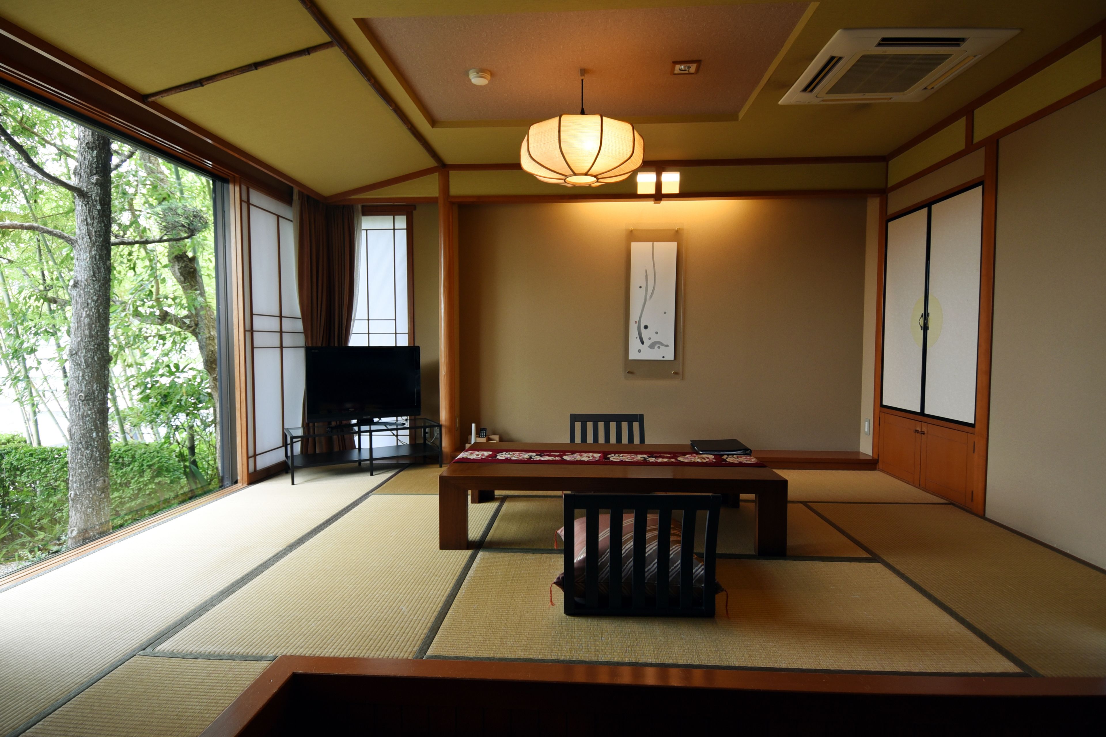 A traditional Japanese room with tatami flooring, a low table, chairs, a television, and sliding doors.