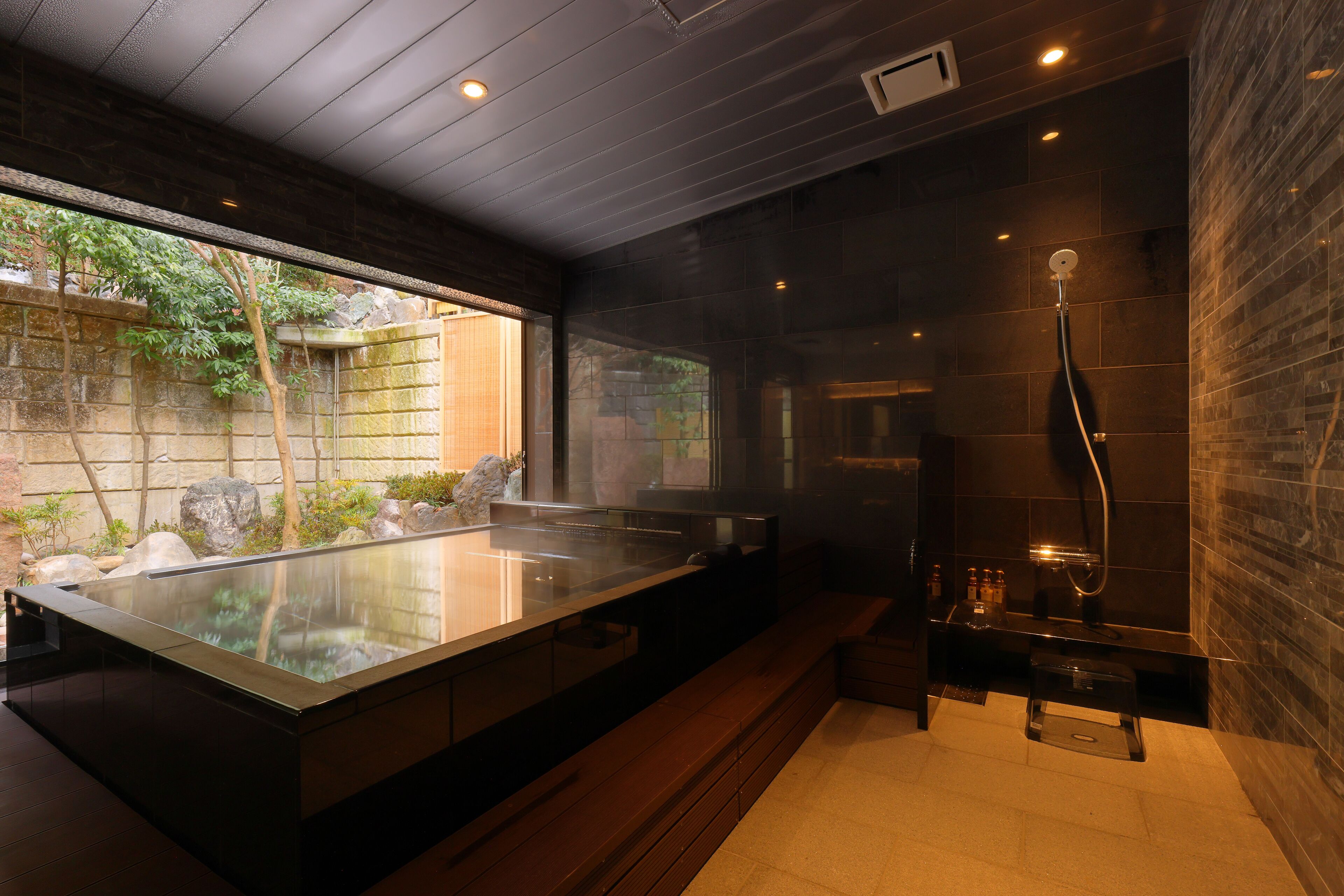A modern bathroom with a glass-enclosed hot tub, a walk-in shower, and a view of a garden.