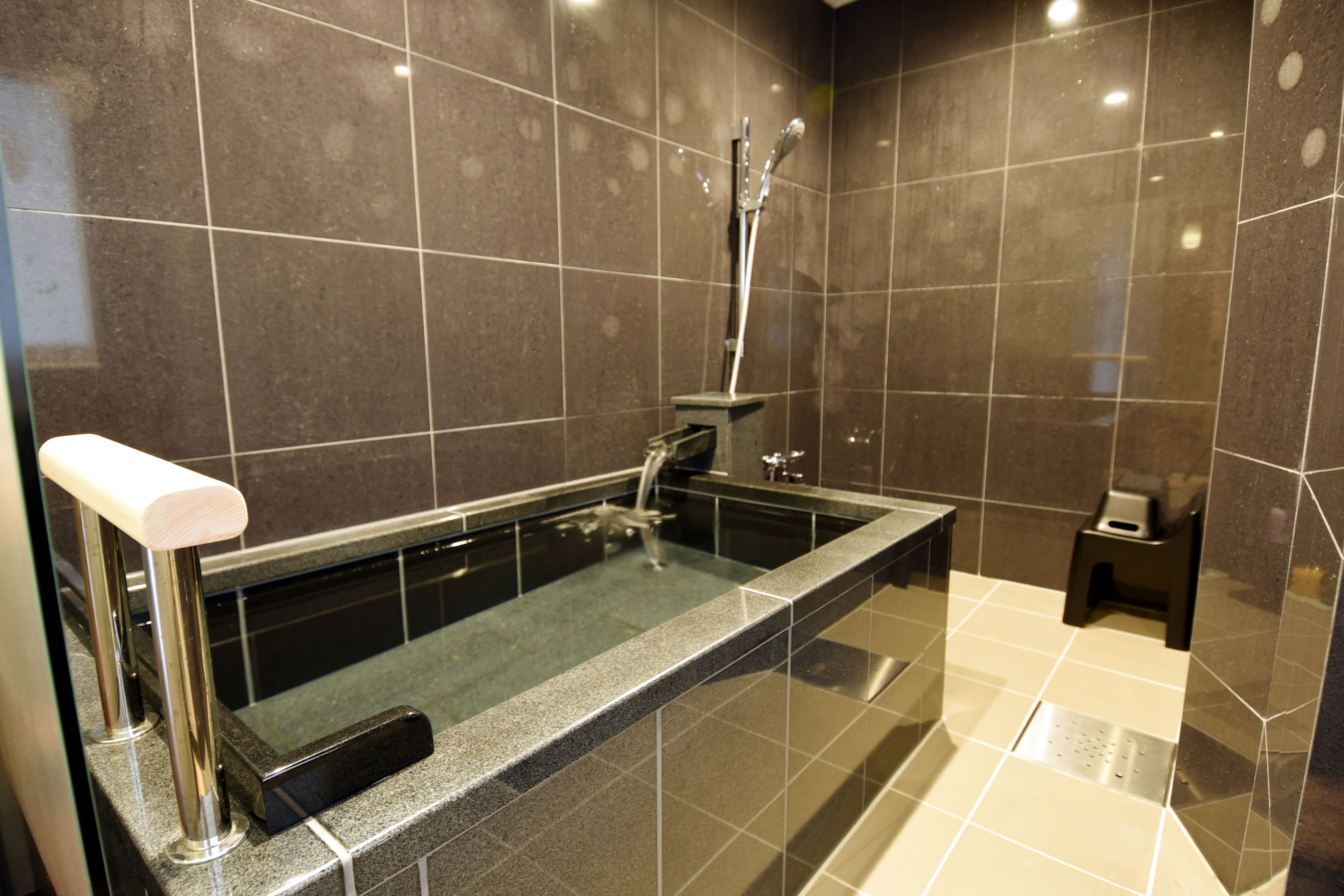 A modern bathroom with a large bathtub, a shower, and a small stool.