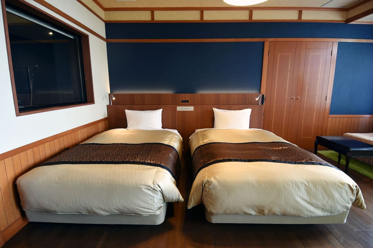 Habitación de hotel con dos camas, cabeceros de madera, un ventanal grande y un armario de madera.