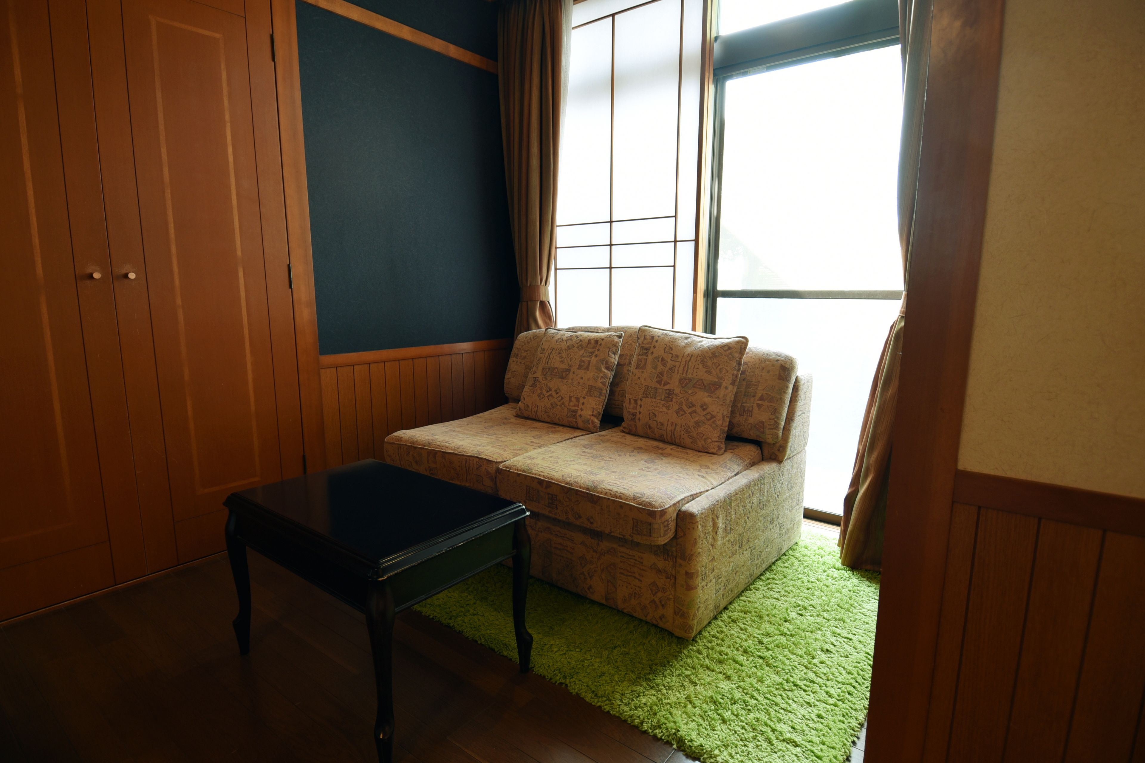 Une pièce avec un mur lambrissé en bois, une moquette verte, un canapé beige orné de coussins à motifs et une table noire.