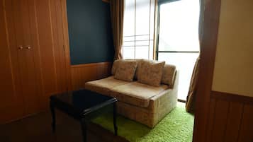Una habitación con pared de paneles de madera, alfombra verde, sofá color beige con cojines estampados y una mesa negra.