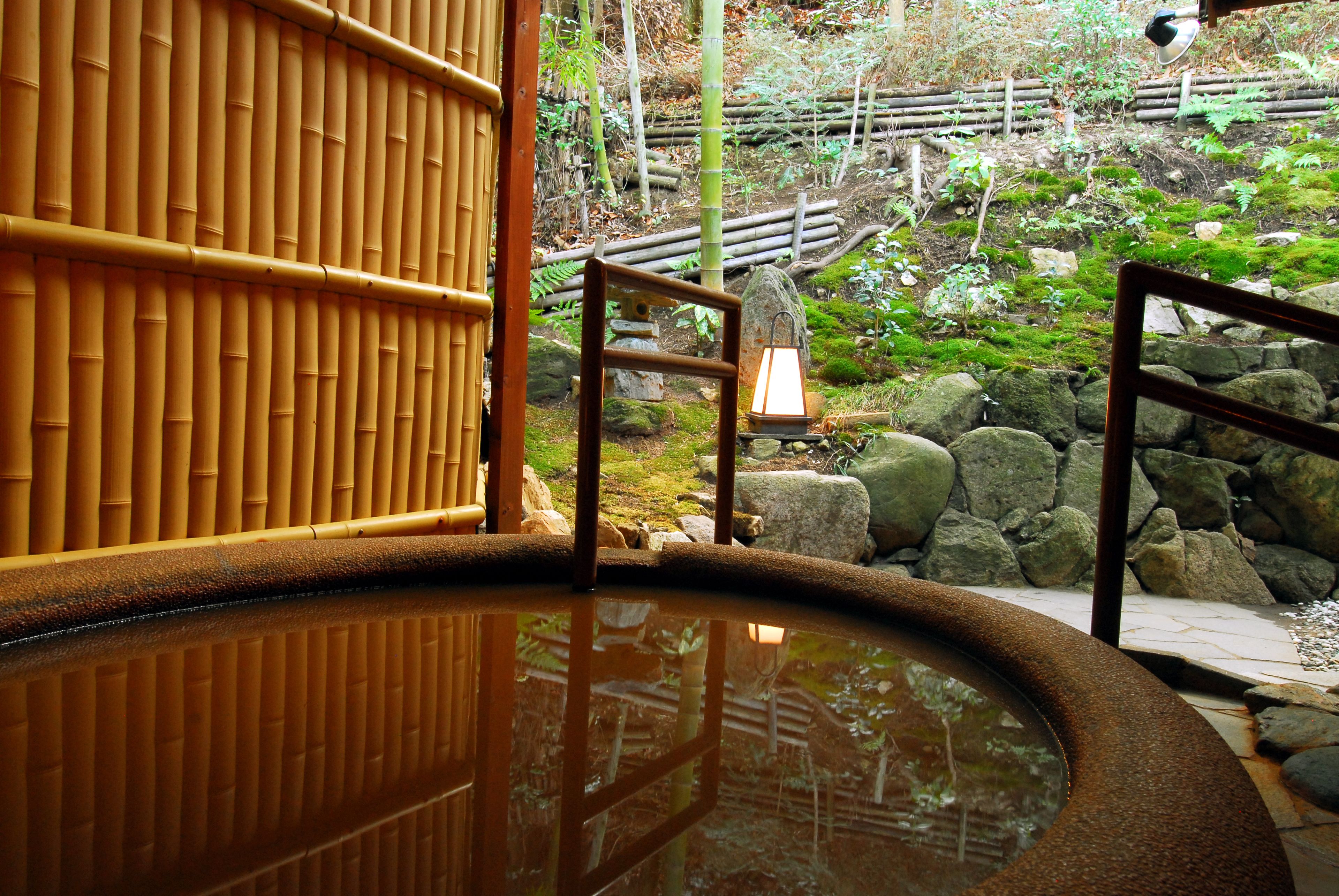 A traditional Japanese onsen with a wooden entrance, a stone lantern, and a rocky garden view.