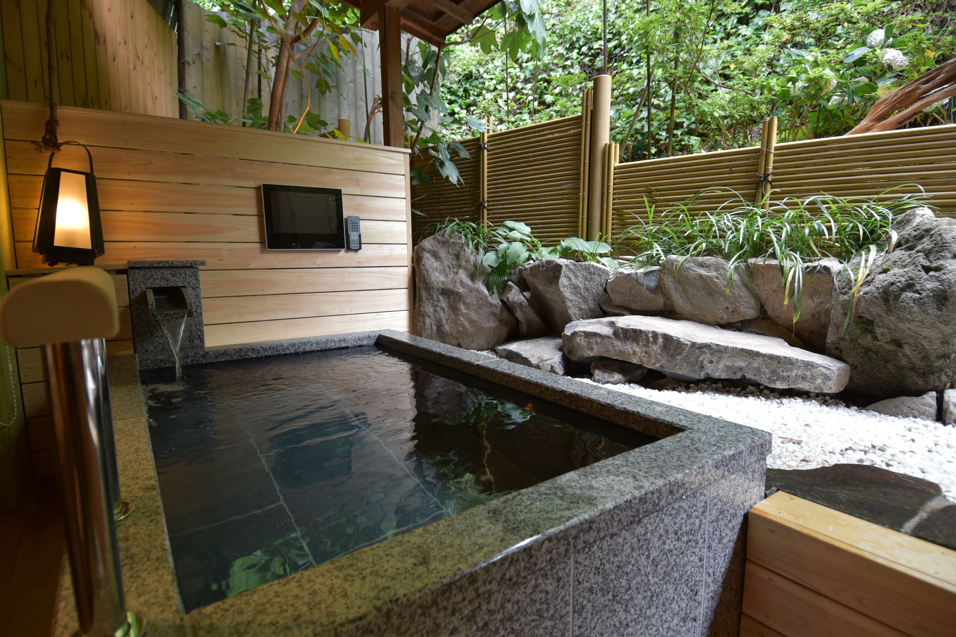 A hot spring area with a wooden wall, a stone seating area, and a small TV screen.