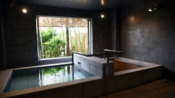 A modern indoor pool area with a view of greenery outside, a seating area with a railing, and a separate hot tub section.