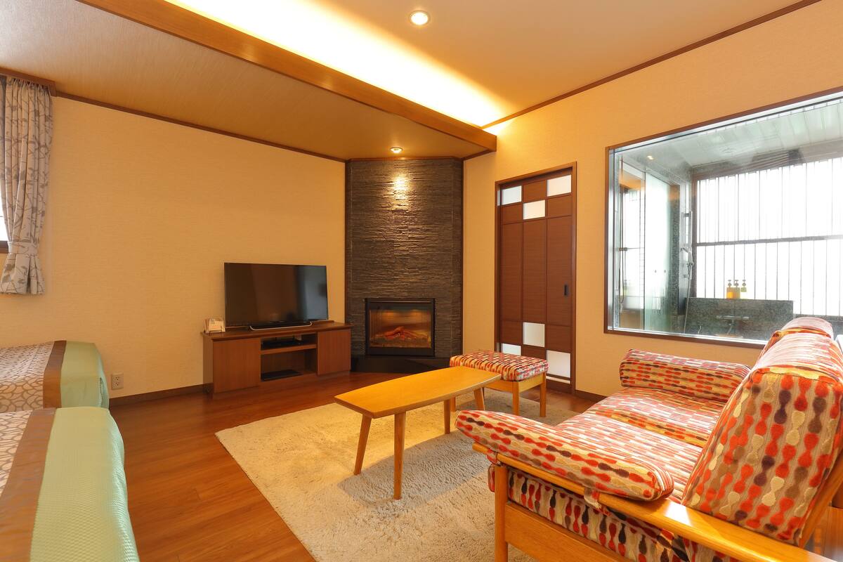 Una sala moderna con un sofá, un televisor de pantalla plana, una chimenea y un ventanal grande.