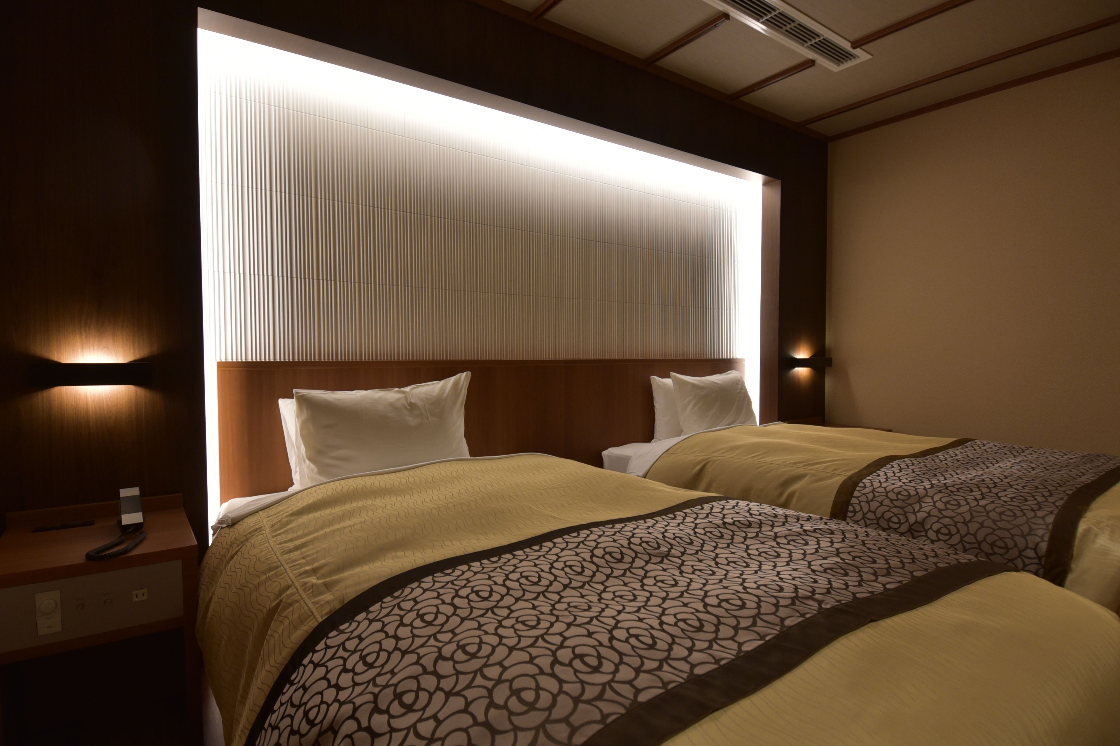 Une chambre d’hôtel avec deux lits, une table de chevet et une tête de lit dotée d’un panneau lumineux.