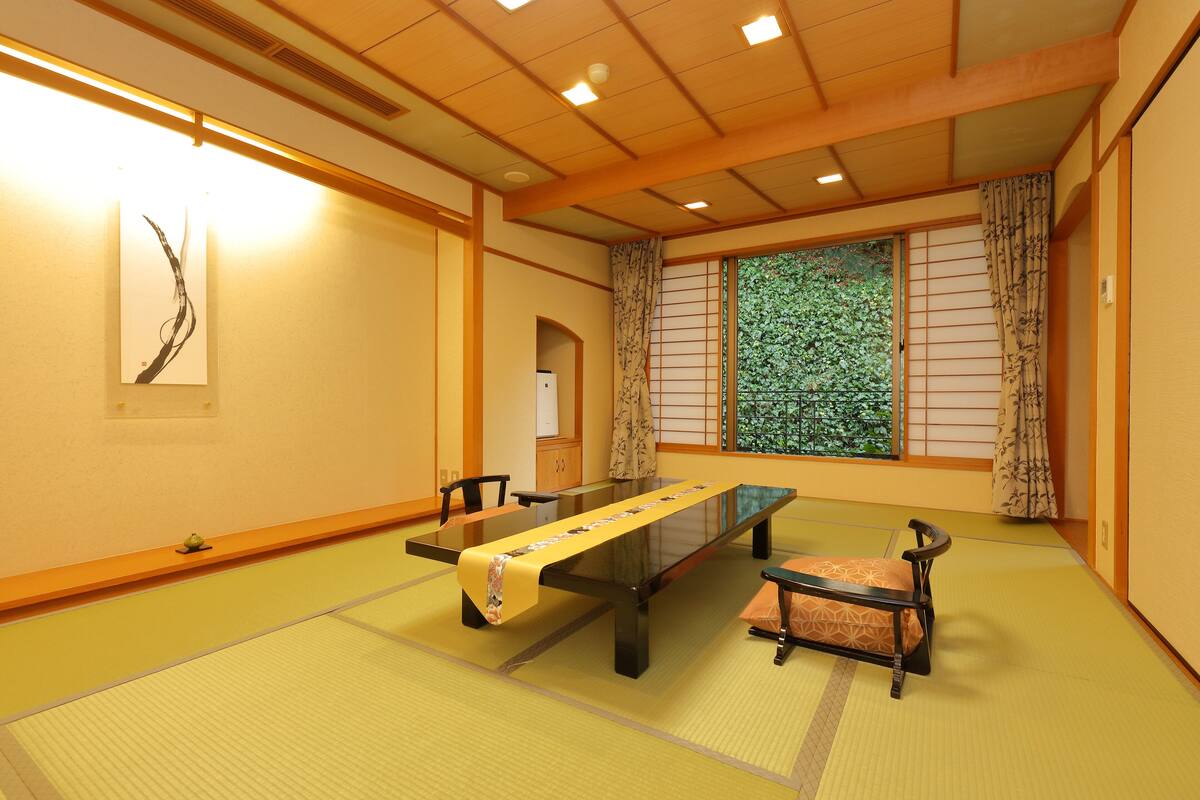 Una habitación japonesa tradicional con suelo de tatami, una mesa baja con cojines y puertas correderas.