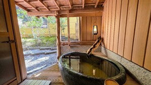 Un onsen japonés tradicional con interiores de madera, una bañera de piedra caliente y un banco de madera.