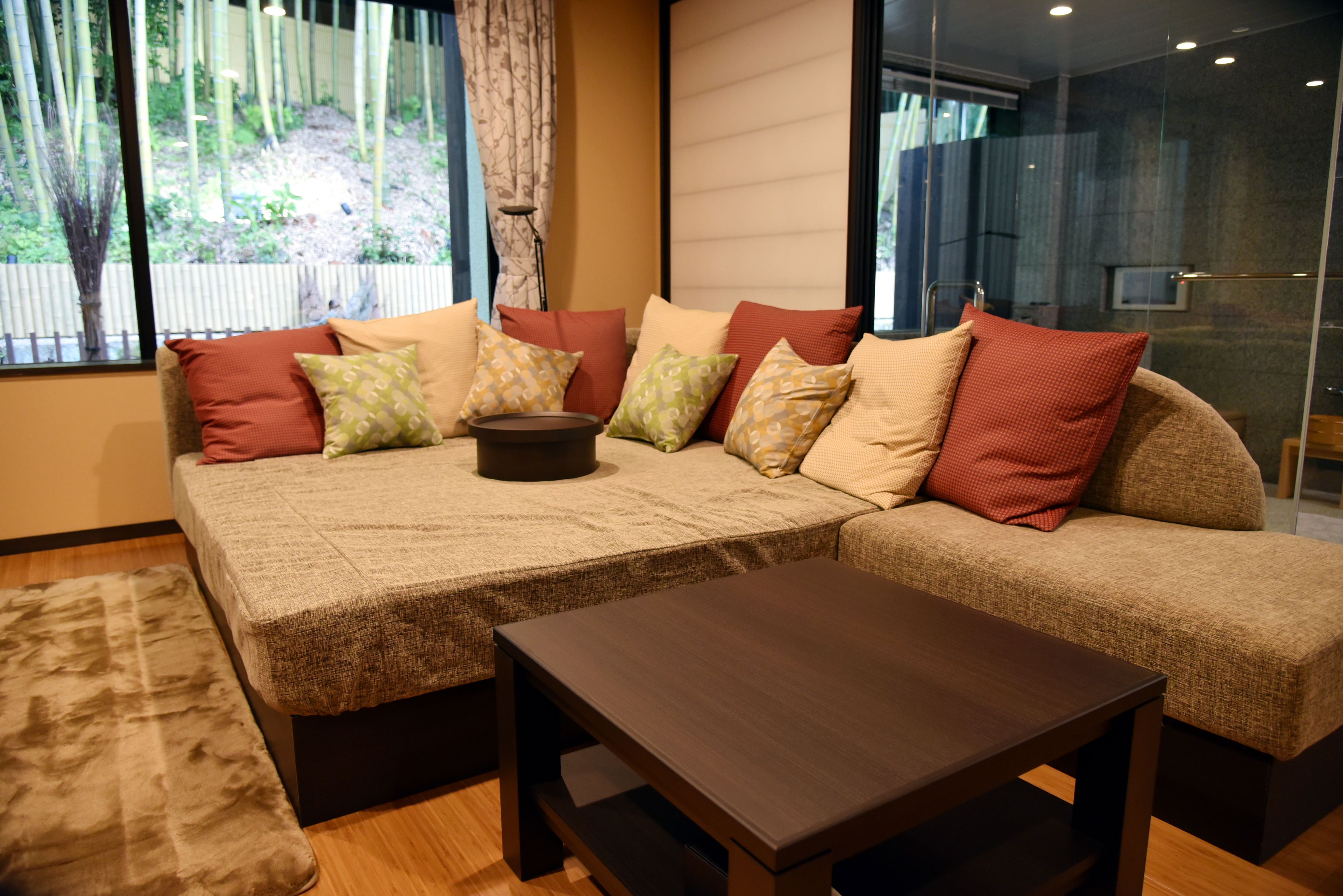 A modern living room with a sectional sofa, a coffee table, and a view of a bamboo garden through large windows.