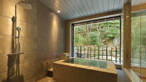 Un baño moderno con una bañera grande, un cabezal de ducha y una ventana que ofrece vistas de la vegetación exterior.