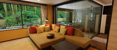 A modern living room with a sectional sofa, a coffee table, and a glass shower area visible through the glass door.