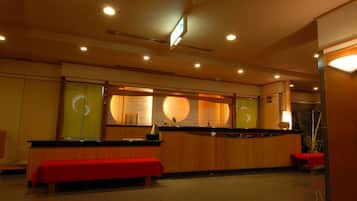 Un hall de hotel con un mostrador de recepción, un banco rojo y una zona de recepción de madera.
