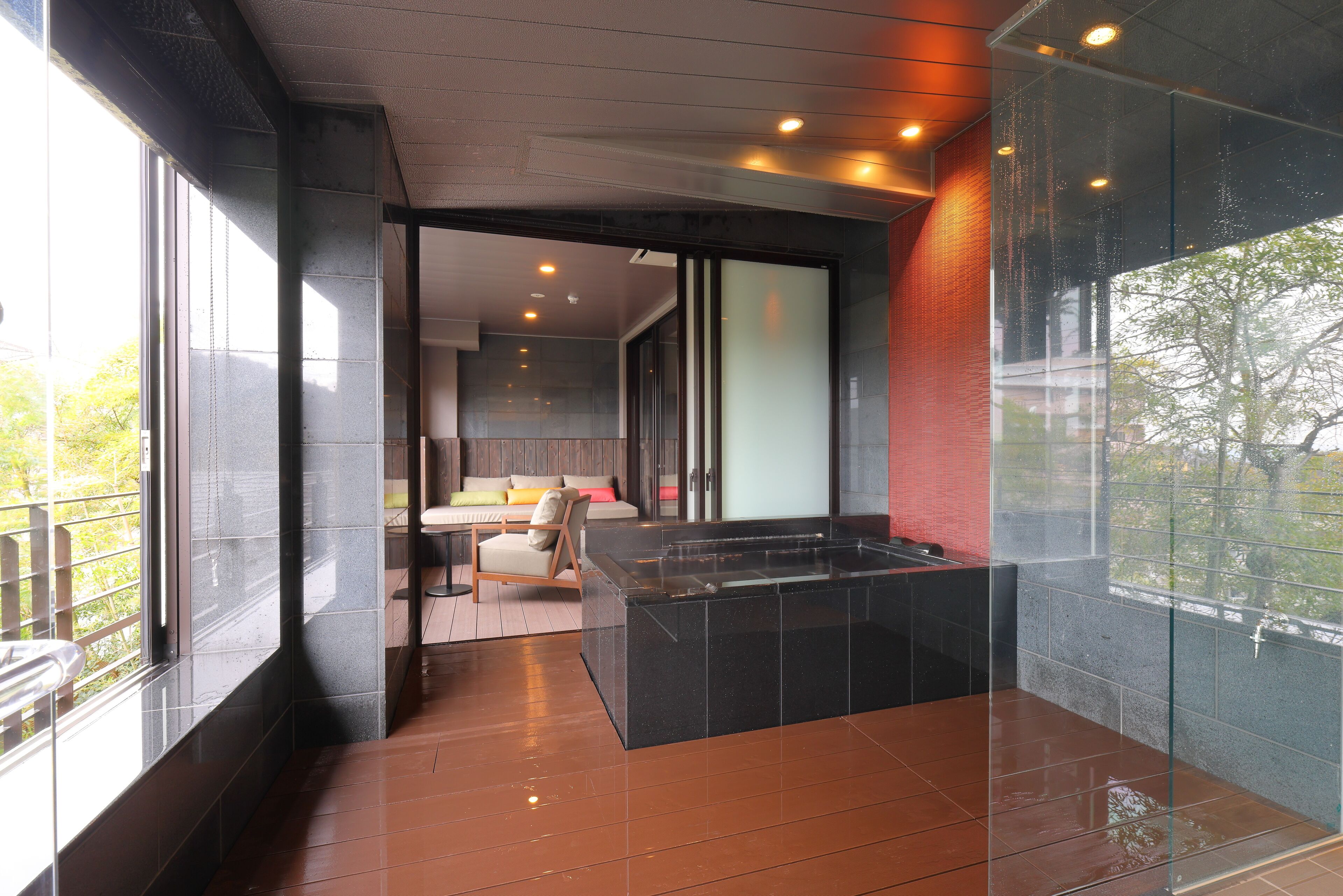 A modern bathroom with a glass-enclosed shower, a bathtub, and a seating area with a sofa and chair.