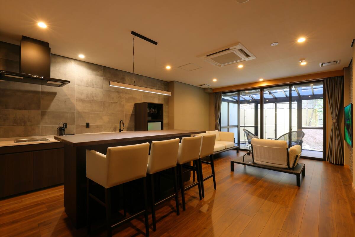 Una cocina moderna con una isla central, taburetes de bar y una zona de estar con sofá y sillones.