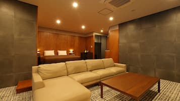 A modern hotel room with a large beige sectional sofa, a wooden coffee table, and a patterned rug.