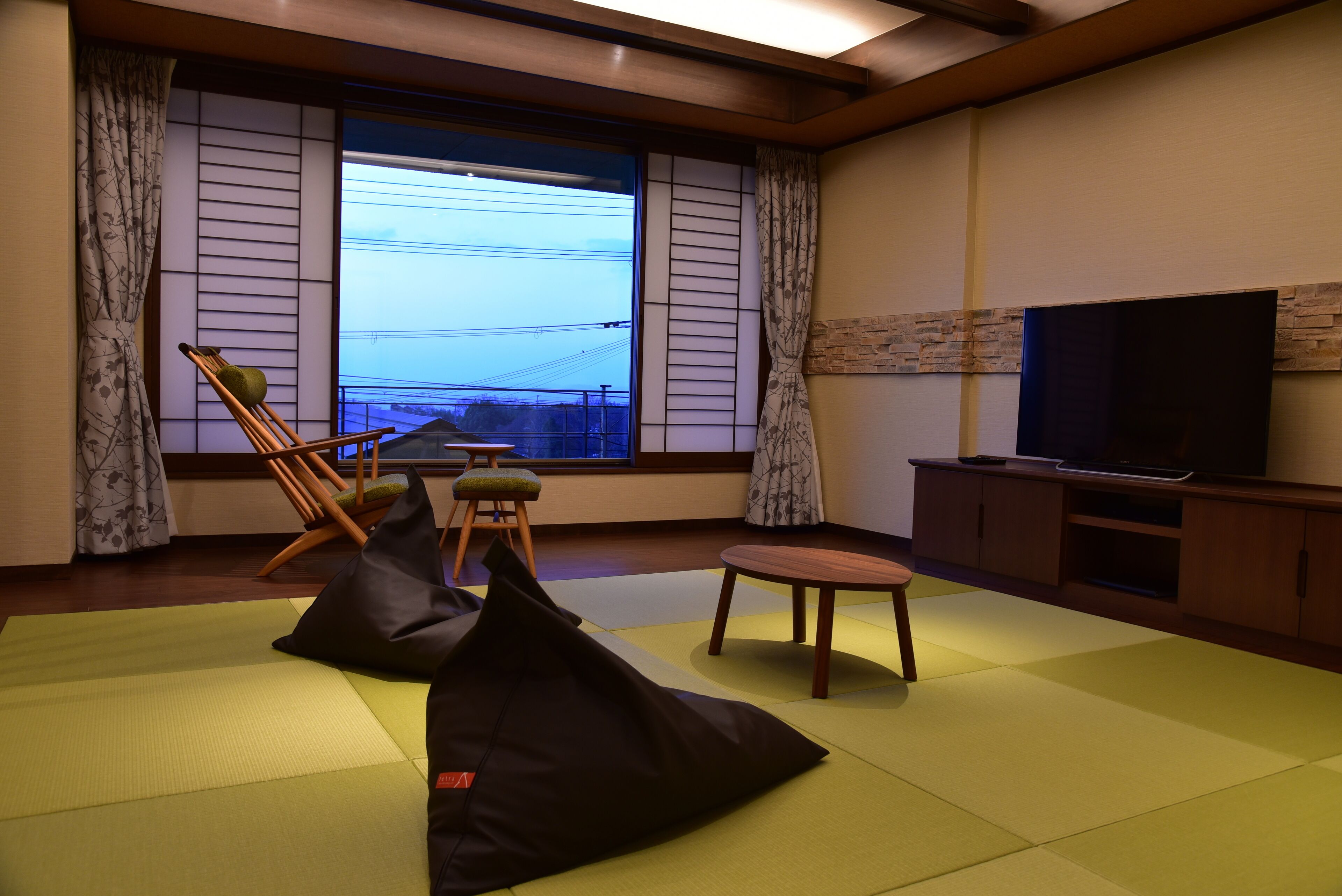 Una habitación con esteras de tatami, un televisor, un armario de madera y vistas al exterior.