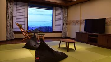 Una habitación con esteras de tatami, un televisor, un armario de madera y vistas al exterior.