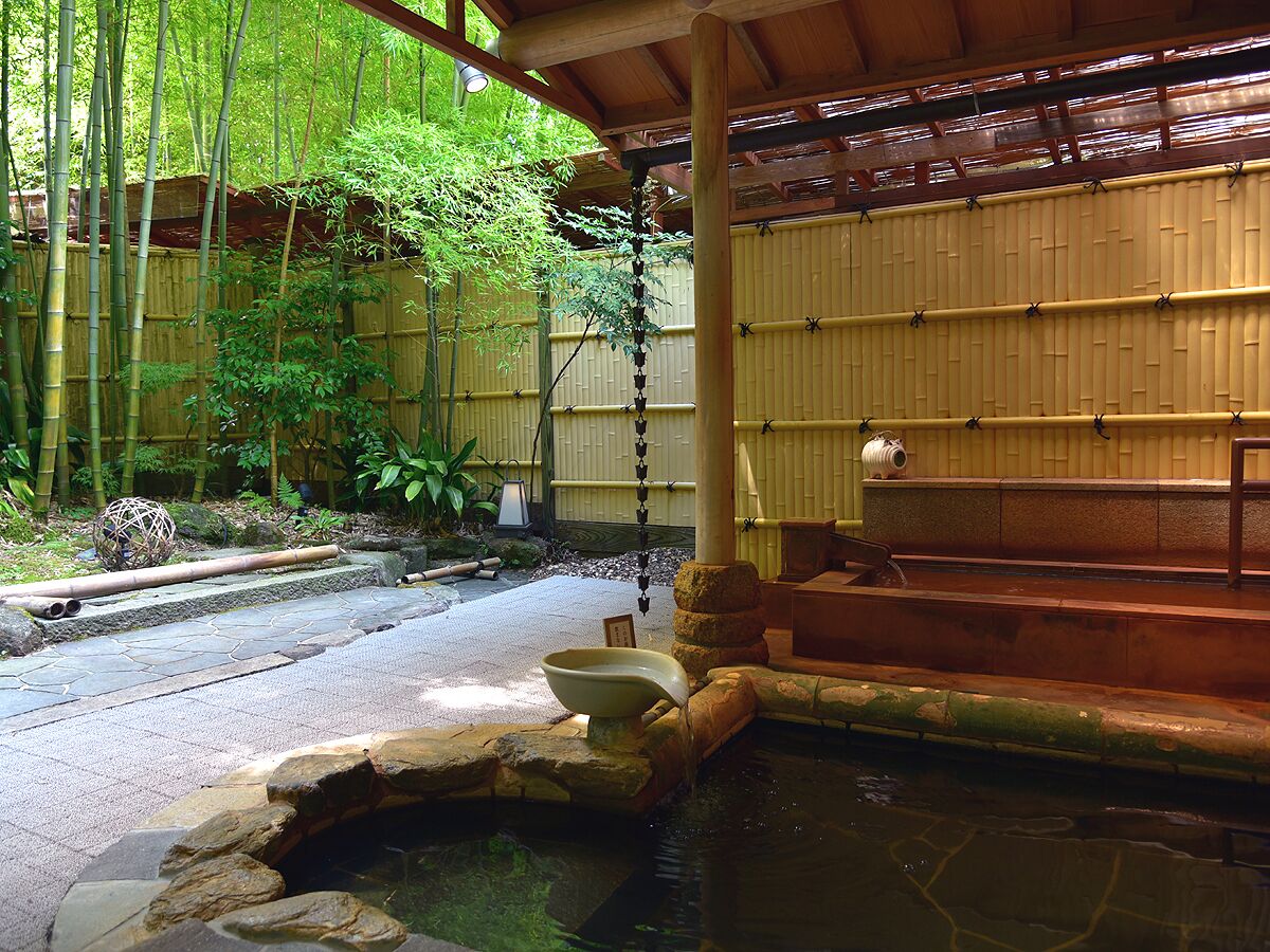 A traditional Japanese onsen with a stone bath, bamboo fence, and a wooden structure.