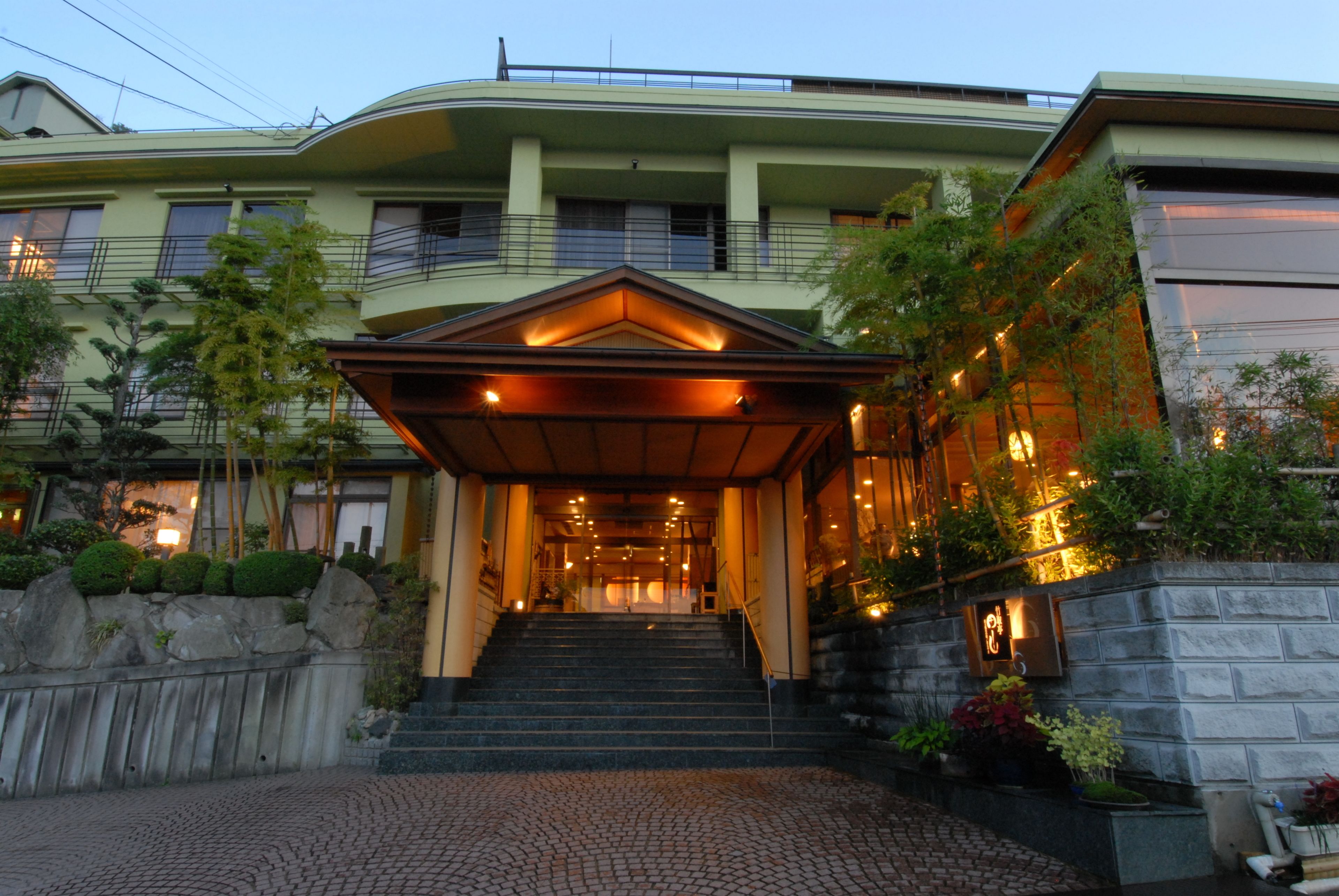 A hotel entrance with a staircase leading to the main building, a covered area, and a stone wall with plants.