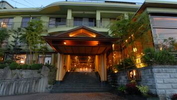 A hotel entrance with a staircase leading to the main building, a covered area, and a stone wall with plants.