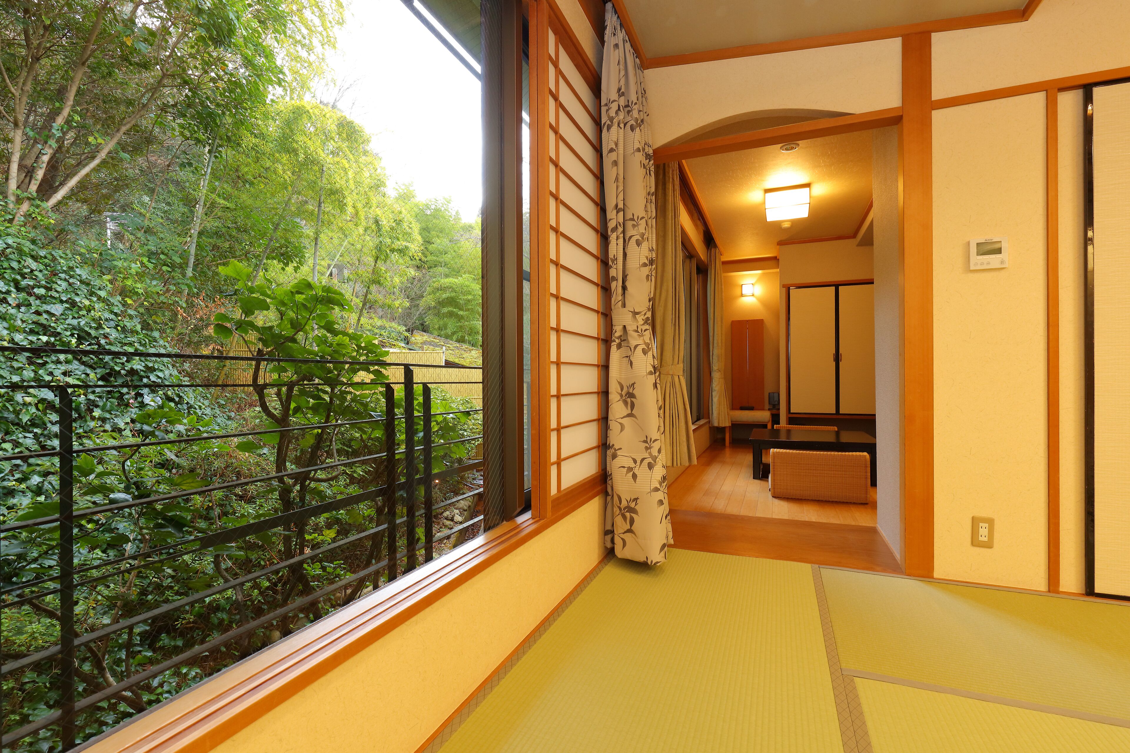 A traditional Japanese room with tatami flooring, a sliding door, and a view of a lush garden.