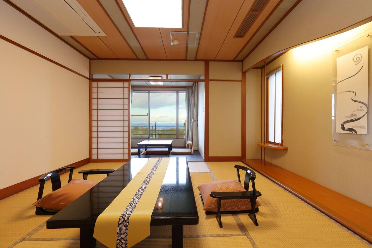 Una habitación tradicional japonesa con suelo de tatami, una mesa baja con cojines y una puerta corredera que da a un balcón.