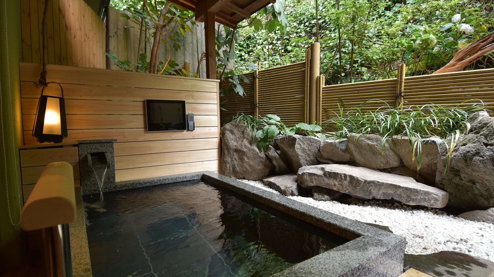 A traditional Japanese onsen with a wooden wall, a stone hot spring, and a rock garden.