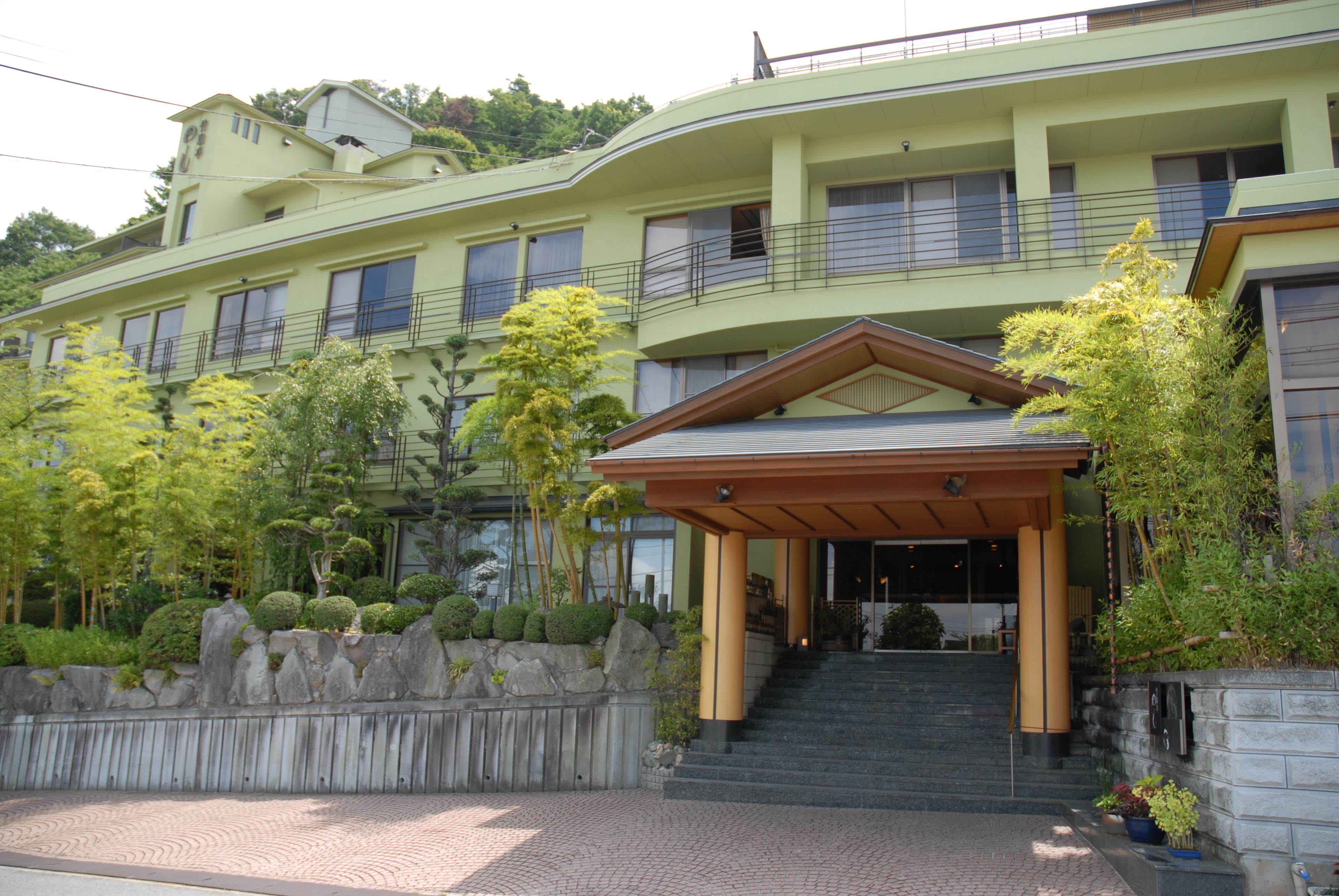 Ein mehrstöckiges Hotel mit überdachter Eingangspartie, einer Steinmauer und umliegendem Grün.