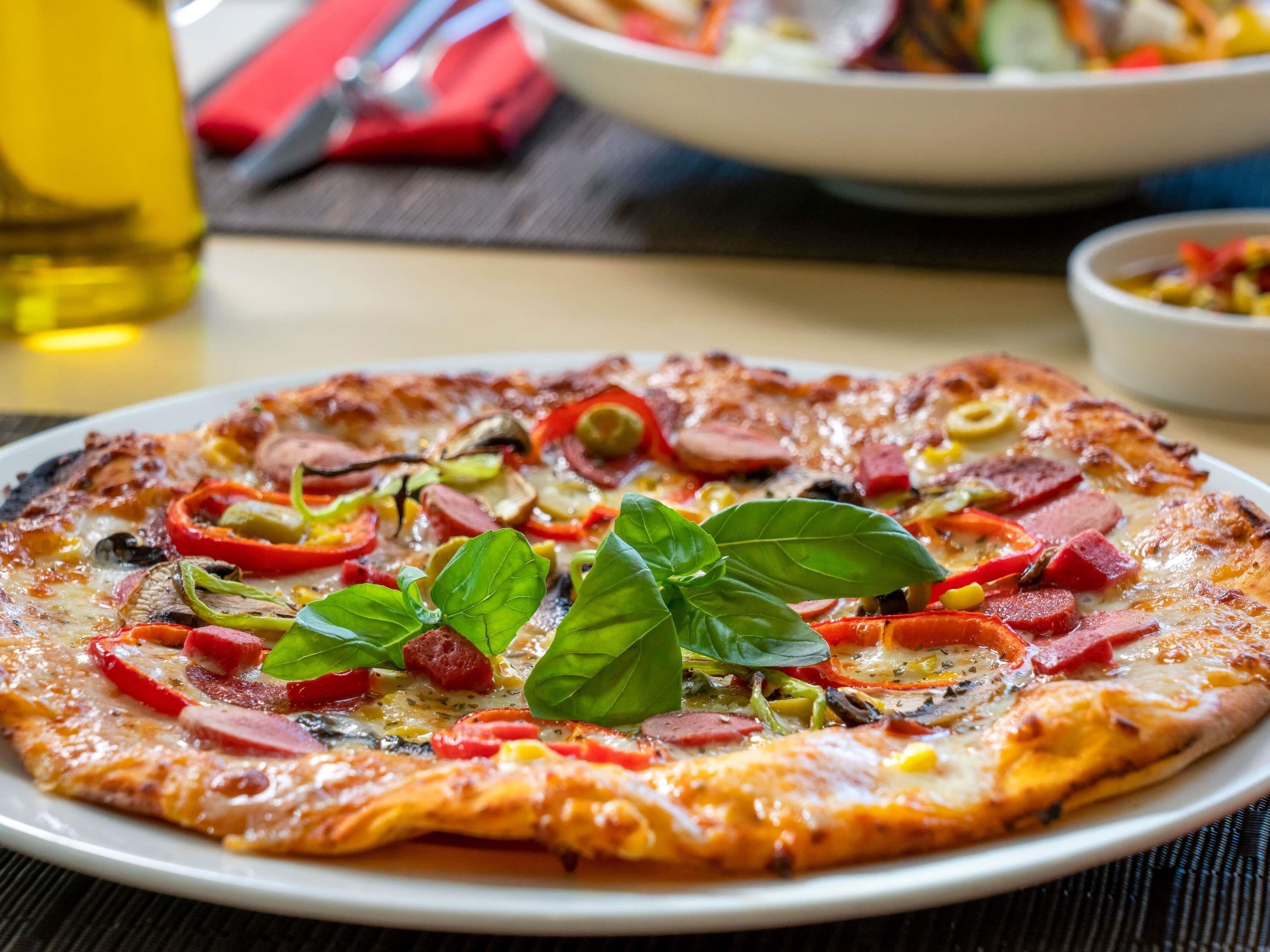 A pizza with various toppings and basil leaves on a plate.