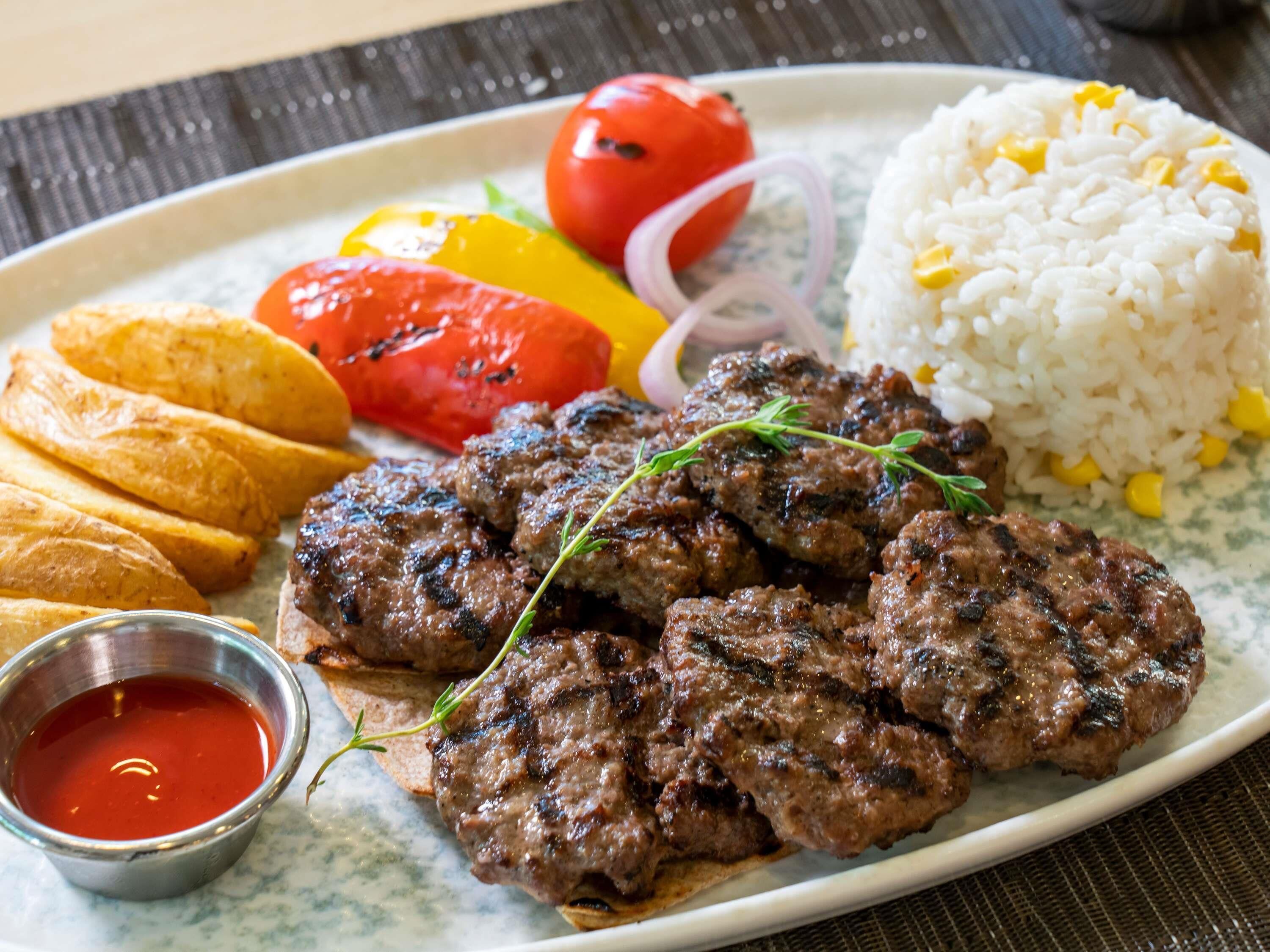 A plate with grilled meat, rice, vegetables, and a small bowl of sauce.