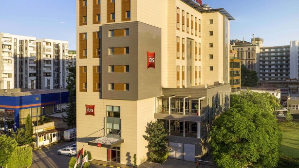 Un hotel moderno con varios pisos, un llamativo letrero que dice "ibis HOTEL" y una entrada de vidrio.