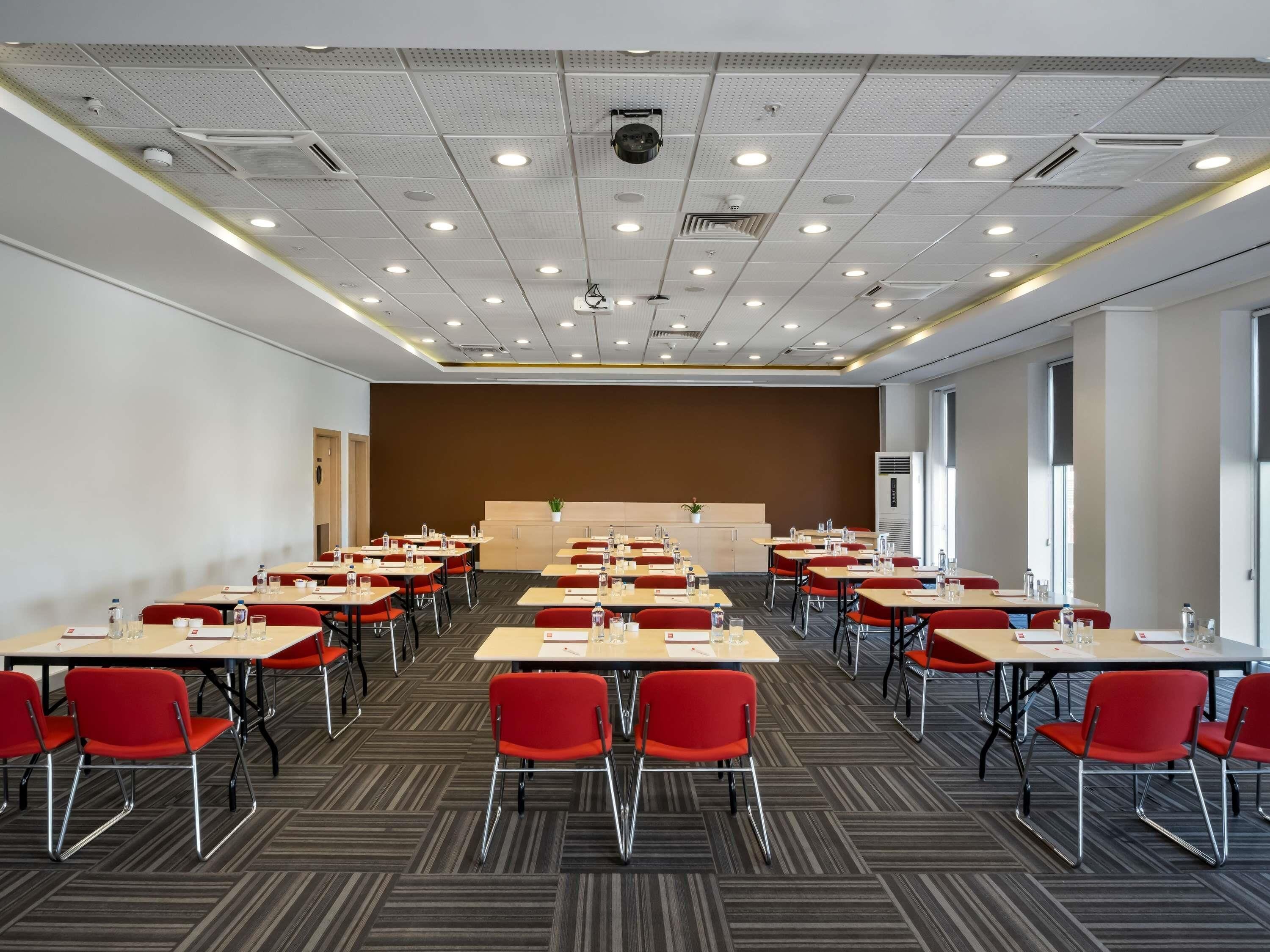 A conference room with multiple tables and chairs, a stage, and a large window.