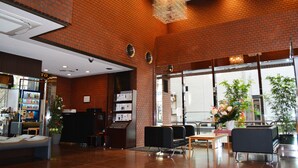 A lobby with a brick wall, seating area, reception desk, and a vending machine. - Grand Central Hotel (Tokyo)