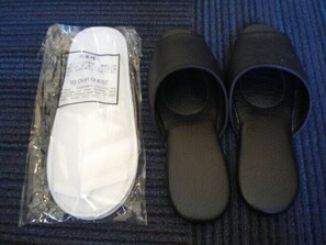 Un par de pantuflas negras y una blanca en un paquete de plástico con una etiqueta.