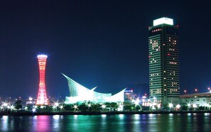 Vista nocturna de un paisaje urbano con edificios iluminados, una torre y un frente marítimo.