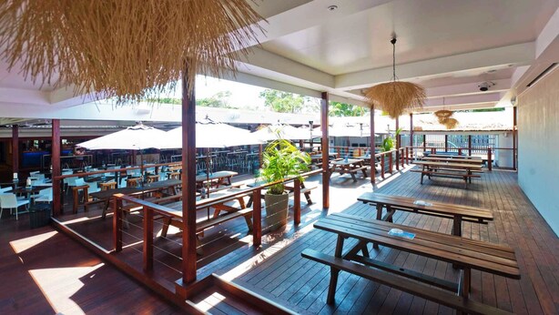 An outdoor dining area with wooden tables and benches, surrounded by umbrellas and potted plants. - Hoey Moey Backpackers - Hostel (Coffs Harbour)
