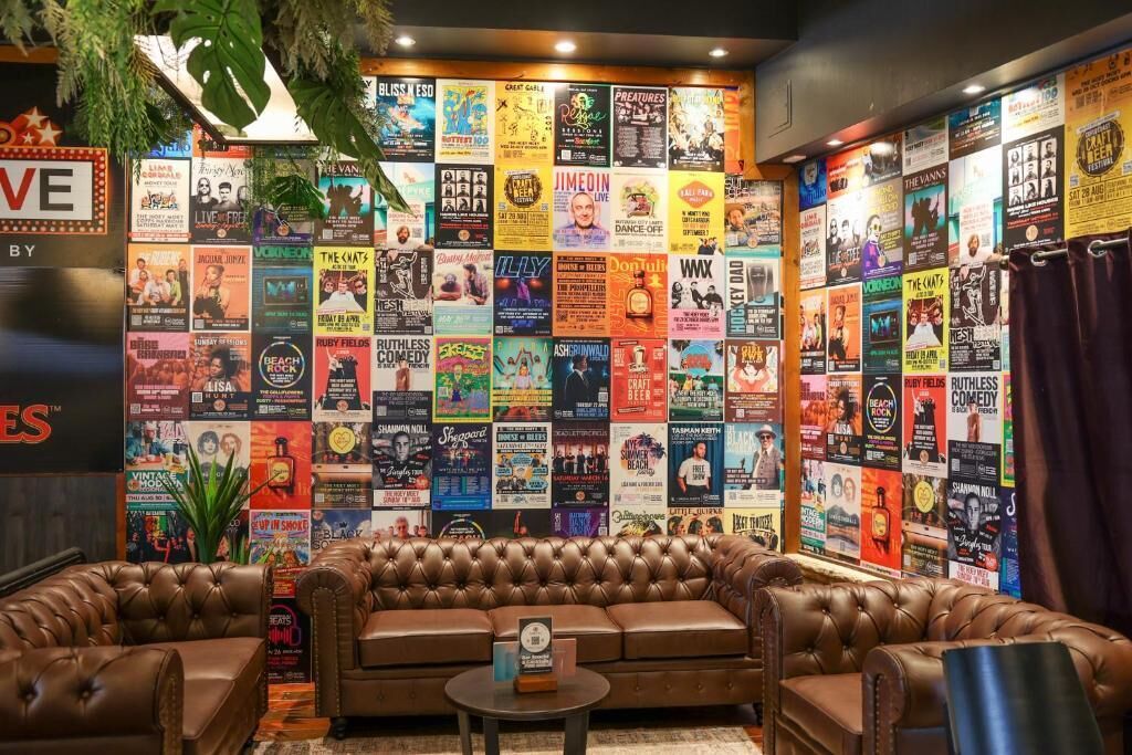 A room with a brown leather couch, a small table, and a wall covered with colorful posters.